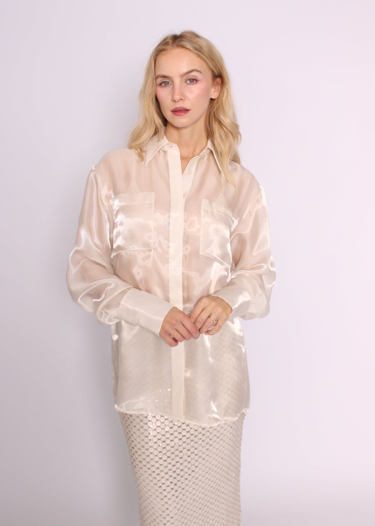 Front view of the BRISTOWE Mirage Shirt in sheer ivory, with long sleeves and chest pockets, worn loose over a sequin skirt