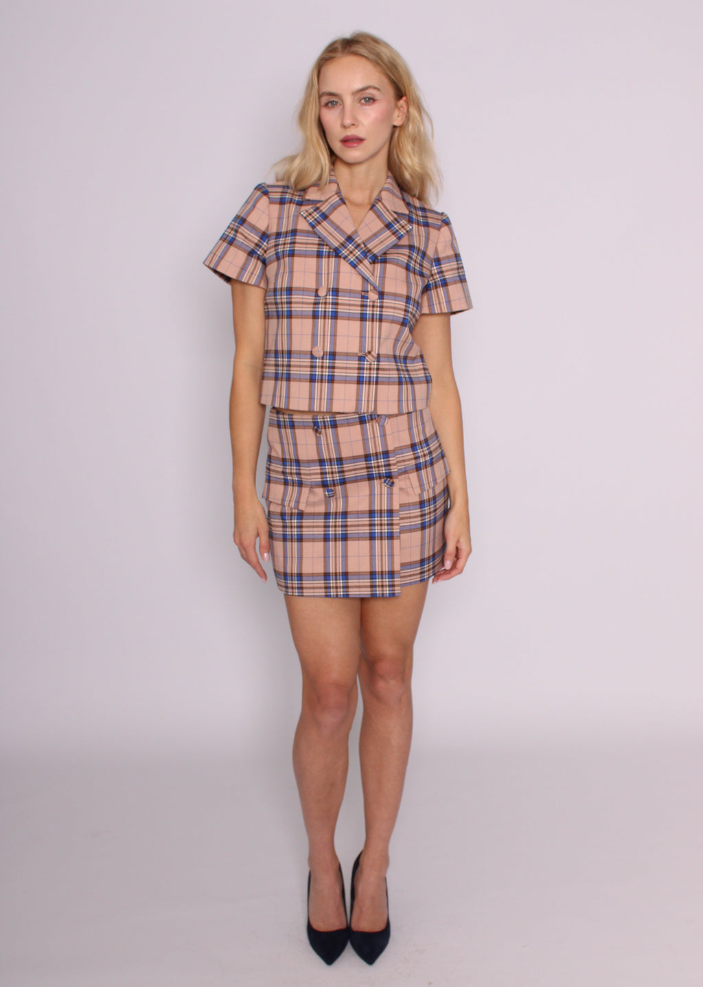 Full-length front view of the BRISTOWE Inez blush tartan mini skirt, styled with the matching top and black heels.
