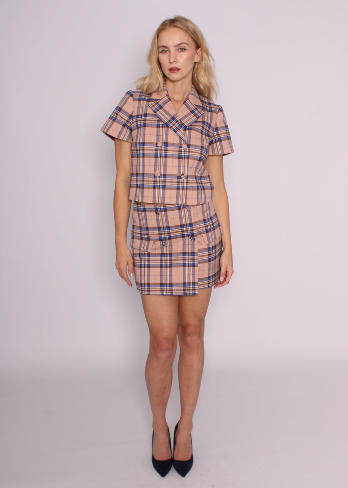 Full-length front view of the BRISTOWE Inez blush tartan mini skirt, styled with the matching top and black heels.
